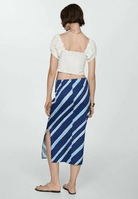 Top court blanc à manches bouffantes ; jupe midi rayée bleue avec une fente latérale. Le matériau semble lisse avec un design fluide.