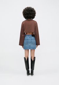 Top marrón cropped de manga larga combinado con una minifalda de mezclilla azul. Botas negras hasta la rodilla, de punta puntiaguda y diseño en forma de V.