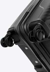 Close-up of black hard-shell suitcase corner showing dual rotating wheels and a zipper.