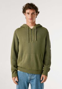 Sudadera verde de punto con un bolsillo delantero, cierre de media cremallera y puños de canalé. El tejido texturizado y el detalle de la capucha realzan el diseño.