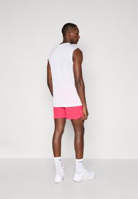 Hvid ærmeløs tanktop kombineret med knaldrøde shorts. Tilbehøret inkluderer hvide sneakers og ankelstrømper med et logo.