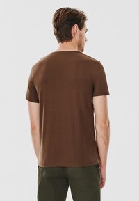 Brązowy T-shirt z krótkim rękawem, z okrągłym dekoltem, gładkim bawełnianym materiałem i luźnym krojem, widoczny z tyłu z jednolitym wzorem.