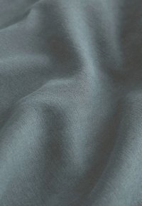 Textil mit Struktur in einem tiefen Teal-Ton, das eine glatte Oberfläche mit subtilen Falten und einem weichen, fließenden Erscheinungsbild aufweist.