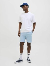 T-shirt blanche à manches courtes, shorts bleu clair, casquette marine, baskets marines avec semelles blanches, chaussettes blanches avec rayures noires.