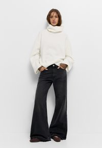 Valkoinen, paksu neulehuppari leveillä hihoilla, yhdistettynä korkeavyötäröisiin, tummiin farkkulegginsseihin. Minimalistinen, rento ilme.