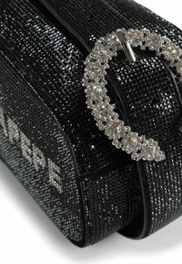 Bolso negro con lentejuelas y una hebilla brillante con acentos de cristal. Presenta una forma alargada y una superficie texturizada. Marca elegante visible.