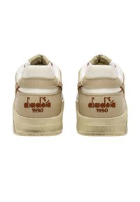 Zapatillas beige con paneles de malla texturizada y detalles de cuero liso. Presenta el logo marrón "diadora 1990" en el talón y una suela de goma.