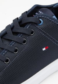 Sneaker a rete blu con punta arrotondata, suola bianca a contrasto e lacci piatti tonali. Presenta un piccolo logo rosso, bianco e blu sul lato.