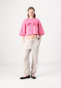 Pink cropped sweatshirt with black text, paired with light beige drawstring trousers, and black flats, presented against a white background.