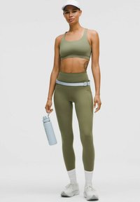 Sportliches Set in Olivgrün, bestehend aus einem kurzen Oberteil und hochgeschnittenen Leggings. Eine hellblaue Wasserflasche und weiße Sneaker sind enthalten.
