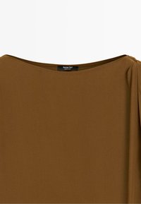 Braune Bluse mit Bootsausschnitt und einem kleinen gerafften Detail an der rechten Schulter, auf der ein Massimo Dutti Etikett zu sehen ist.