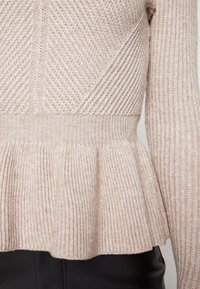 Helles beiges Strickpullover mit Peplum-Saum, geripptem Textur sowie vertikalen und diagonalen Stichmustern.