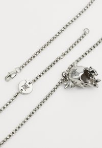 Ασημένιο μεταλλικό κολιέ με σχέδιο αλυσίδας και διακοσμητικό κρεμαστό φrog. Ο κρεμαστός φrog περιλαμβάνει περίπλοκες λεπτομέρειες και κλείσιμο με κούμπωμα.