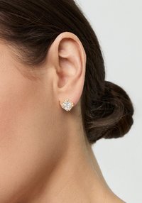 Złote kolczyki wkręty z centralnym, przezroczystym kamieniem z cyrkonii, otoczonym mniejszymi przezroczystymi kamieniami w kwiatowym wzorze.