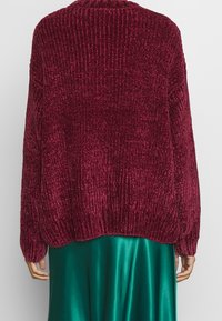 Bordó žebrovaný pletený kardigan s volným střihem, dlouhými rukávy a kulatým výstřihem, doplněný zelenou saténovou sukní.