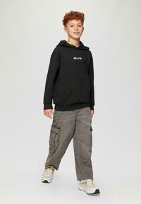 Felpa nera con cappuccio e tasca frontale, con logo bianco "SLVR", abbinata a pantaloni cargo grigi con tasche laterali e sneakers chiare.