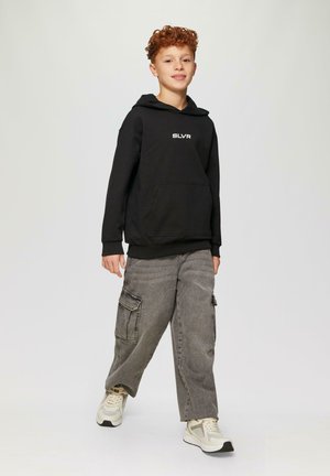 Zwarte hoodie met buidel en witte "SLVR" logo, gecombineerd met grijze cargobroek met zijzakken, en lichte sneakers.