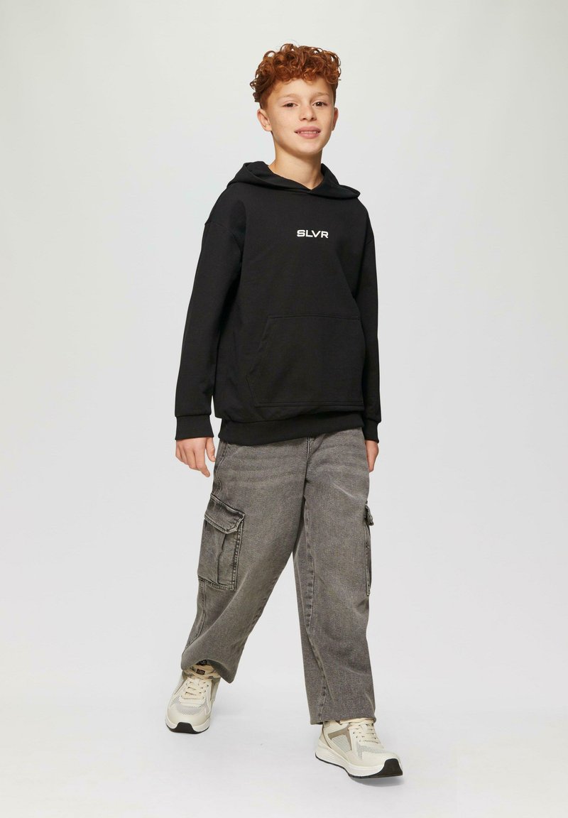 Felpa nera con cappuccio e tasca frontale, con logo bianco "SLVR", abbinata a pantaloni cargo grigi con tasche laterali e sneakers chiare.