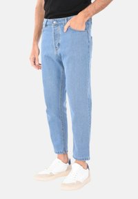 Jeans in denim azzurro chiaro con vita alta, leggermente affusolati alla caviglia, due tasche anteriori e chiusura con zip. Abbinati a sneaker bianche.