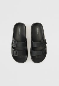 Black slide sandals with two adjustable buckle straps, made of smooth plastic material, featuring a contoured footbed and flat sole.