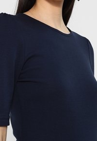 Marinblå kortärmad topp i mjuk, stretchy tyg. Har en rundad halsringning och en figurnära siluett, lämplig för olika stilar.