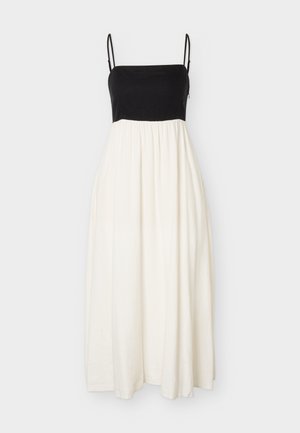 Μαύρο αμάνικο τοπ με λεπτές τιράντες και λευκή ροή μακριά φούστα σε απλό φόντο.