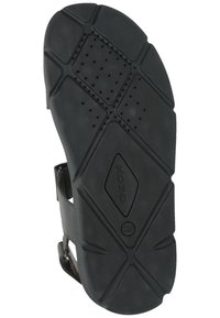 Semelle de sandale en caoutchouc noir avec un motif texturé et des perforations ; présente un logo au centre et une forme contoured pour soutenir le pied.