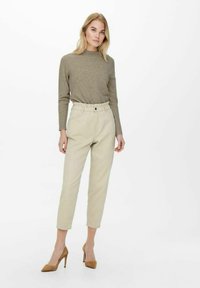 Pantaloni beige a vita alta con una vestibilità rilassata, abbinati a un maglione lavorato a maglia di un leggero verde oliva e tacchi a punta marroni.