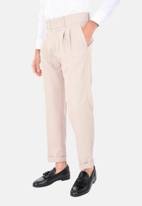 Pantaloni beige plissettati con cintura larga, due bottoni, tasche laterali e risvolti, abbinati a mocassini in pelle nera.