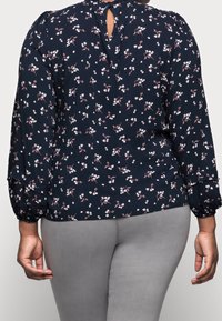 Marinblå blus med blommönster, långa puffärmar, nyckelhål på baksidan och små vita och rosa blommor. Slätt, lätt material.