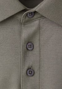 Gros plan sur le devant d'un polo en maille gris avec trois boutons noirs et un col pointu.