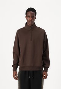 Brun, højhalset sweatshirt med en halv lynlås; afslappet pasform, blød tekstur, ribbede manchetter og kant, båret over mørke, løstsiddende bukser.