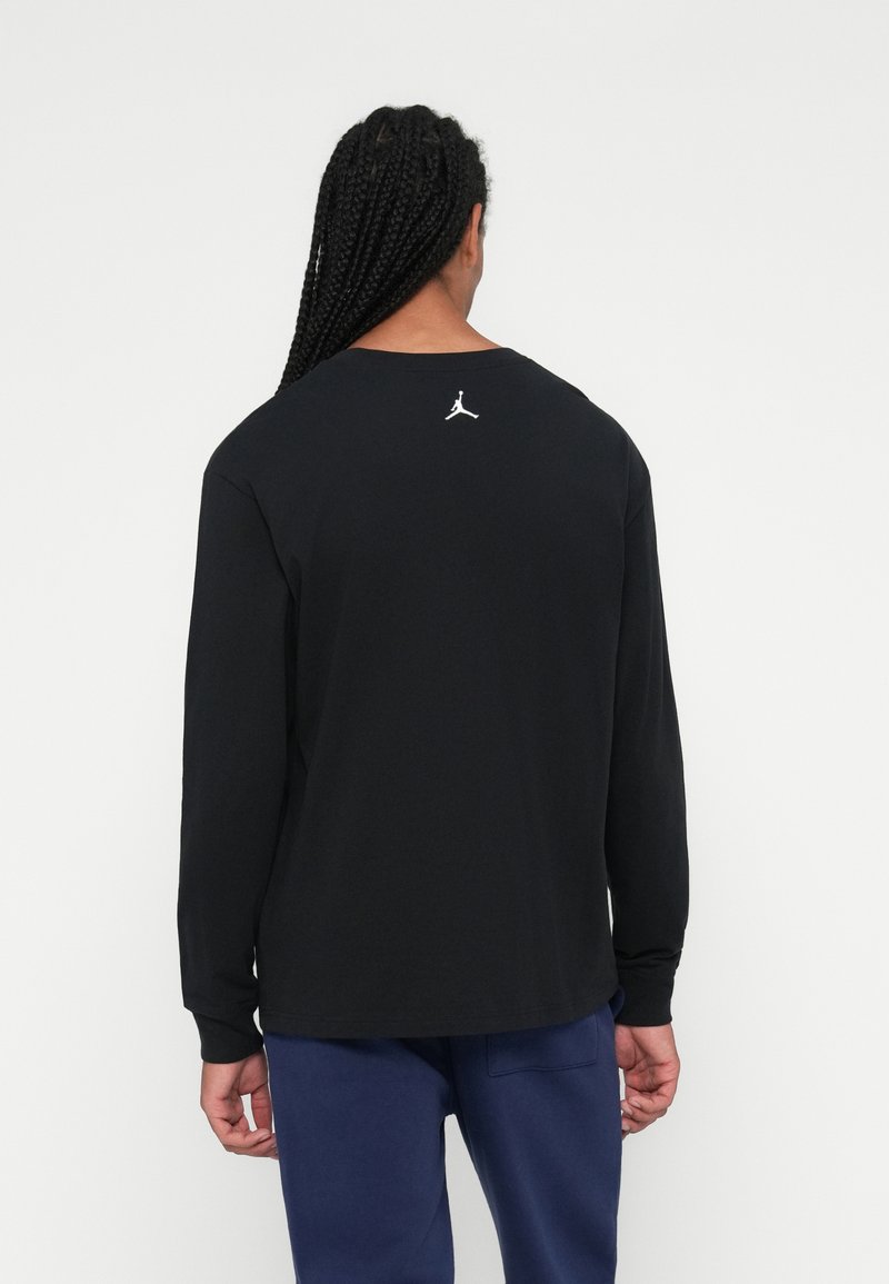 Schwarzes Langarmshirt mit Rundhalsausschnitt und einem weißen Jordan-Logo auf dem oberen Rücken. Hergestellt aus weichem Baumwollstoff, entspannte Passform.