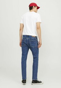 Jeans subțiri din denim albastru cu talie medie, având un petic din piele pe spate, asortați cu un tricou alb simplu și adidași negri.
