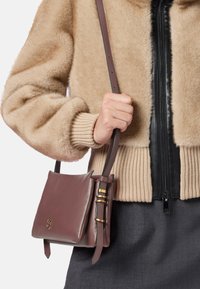 Borsa a spalla in pelle marrone con una finitura liscia, dettagli in hardware dorato e un design piatto. La tracolla è regolabile e attaccata con clip.