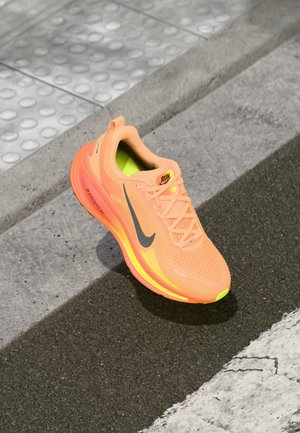 Baskets de sport orange avec tige en mesh respirant, accents gris réfléchissants et semelle jaune. Design léger avec un logo Nike audacieux.