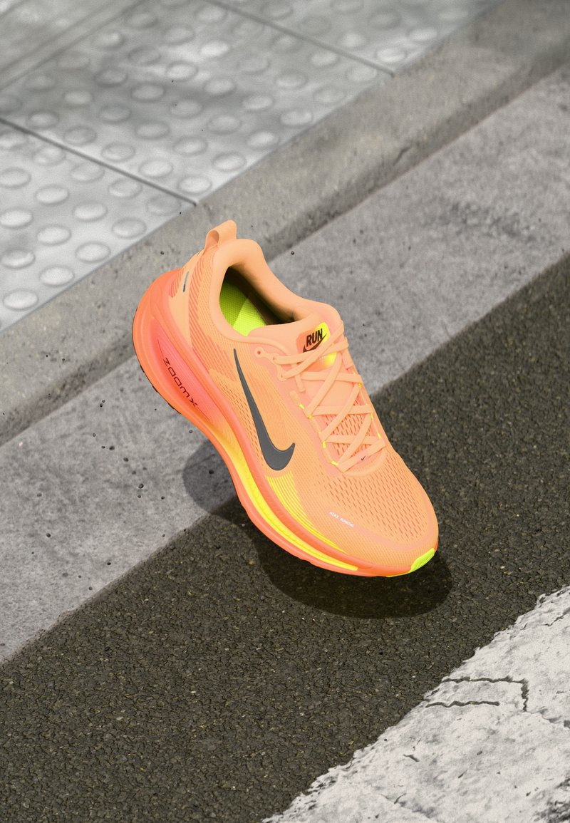 Orange idrottssko med andningsbart mesh-övre, reflekterande grå detaljer och en gul sula. Lättviktig design med djärv Nike-logotyp.