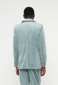 Saten blejzer u mekoj plavoj boji sa strukturnim ovratnikom, jednim prorezom pozadi i detaljima dugmadi na rukavima. Tekstura sa glatkim završetkom.