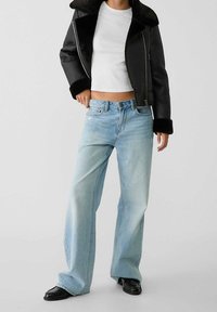 Giacca nera foderata in pelliccia sintetica con revers ampi, top bianco corto e jeans larghi blu chiaro. A completare il look, scarpe nere flat.