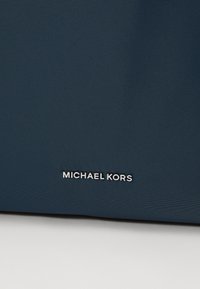 Sac à main en tissu bleu marine avec une texture lisse et un logo argenté "MICHAEL KORS" en bas.
