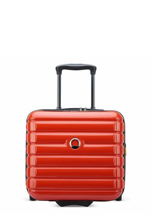 Valise rigide rouge avec texture à rainures horizontales, poignée noire et fermeture éclair. Présente un logo rond à l'avant. Design compact et robuste.