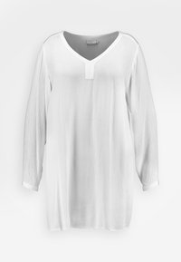 Weiße Bluse mit langen Ärmeln, V-Ausschnitt und durchgeknöpftem Vorderteil. Sie hat einen strukturierten Stoff und manschettenartige Ärmel mit rohen Kanten.