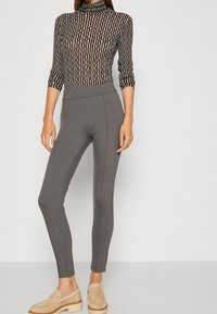 Grå stretchleggings med hög midja, kombinerat med en långärmad topp i svart och beige randig design. Slätt tyg med figurnära passform.