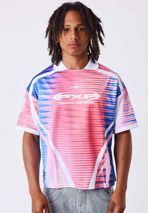 Jeune homme avec des dreadlocks mi-longs portant un maillot de sport coloré rose, bleu et blanc avec le logo "PXP Change the Game".