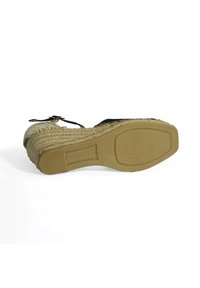Sandale compensée avec un dessus tissé en beige et détails noirs, semelle en corde texturée et semelle en caoutchouc avec un motif de grip.