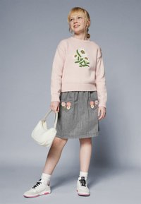 Light pink knitted sweater with floral embroidery, gray pleated skirt with heart-shaped pockets, white fluffy handbag, and sneakers with pink accents.