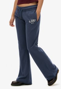 Granatowe dresy o luźnym kroju, z regulowanym paskiem w talii, z białym napisem "S.DRY N.Y.C" na lewej udzie.