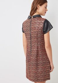 Vestido multicolorido con una tela texturizada y estampada con motivos florales, mangas cortas de cuero negro y cremallera en la parte trasera.