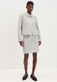 Grijze wolmix cropped jack met een kraag, gecombineerd met een bijpassende kokerrok tot de knie. Gladde textuur en minimalistisch ontwerp. Zwarte ballerina's met studs.