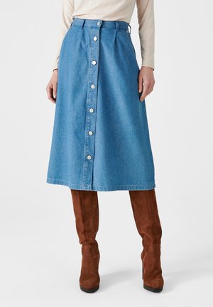 Lichtblauwe denim midi-rok met een sluiting met knopen aan de voorkant, brede tailleband en een rechte snit. Gekoeld met bruine suède laarzen tot over de knie.